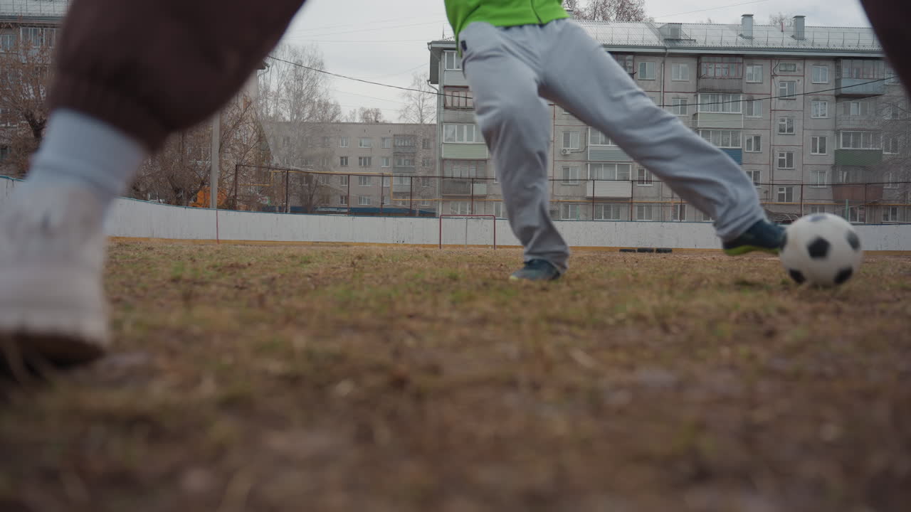운동선수가 고르지 못한 필드를 빠르게 가로지르고, 한 축구 선수가 울퉁불퉁한 주거 지역 표면에서 앞으로 돌진하며, 결연한 축구 선수가 고르지 못한 도시 운동장에서 골망을 향해 나아가요.