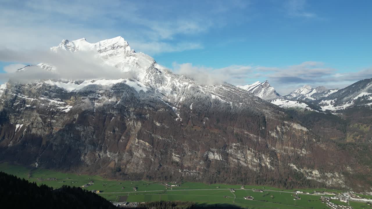 estableciendo una visión general aérea de los escarpados acantilados erosionados y la cresta del pico de la montaña cubierta de nieve y la pintoresca aldea rural