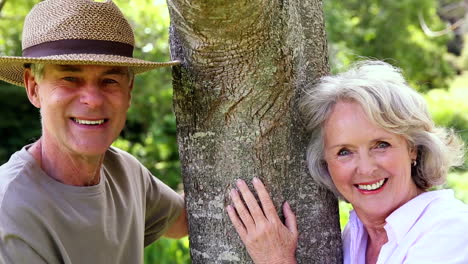 retired couple leaning against tree smiling at each other