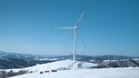 gigantic wind turbine spins against clear sky on mountain summit with mountains range in background at daegwallyeong sky ranch, korea