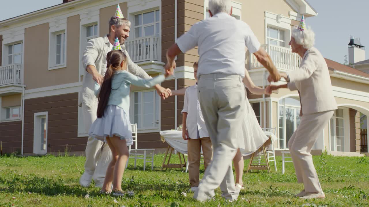 Famiglia che balla in cerchio attorno al festeggiato all'aperto.