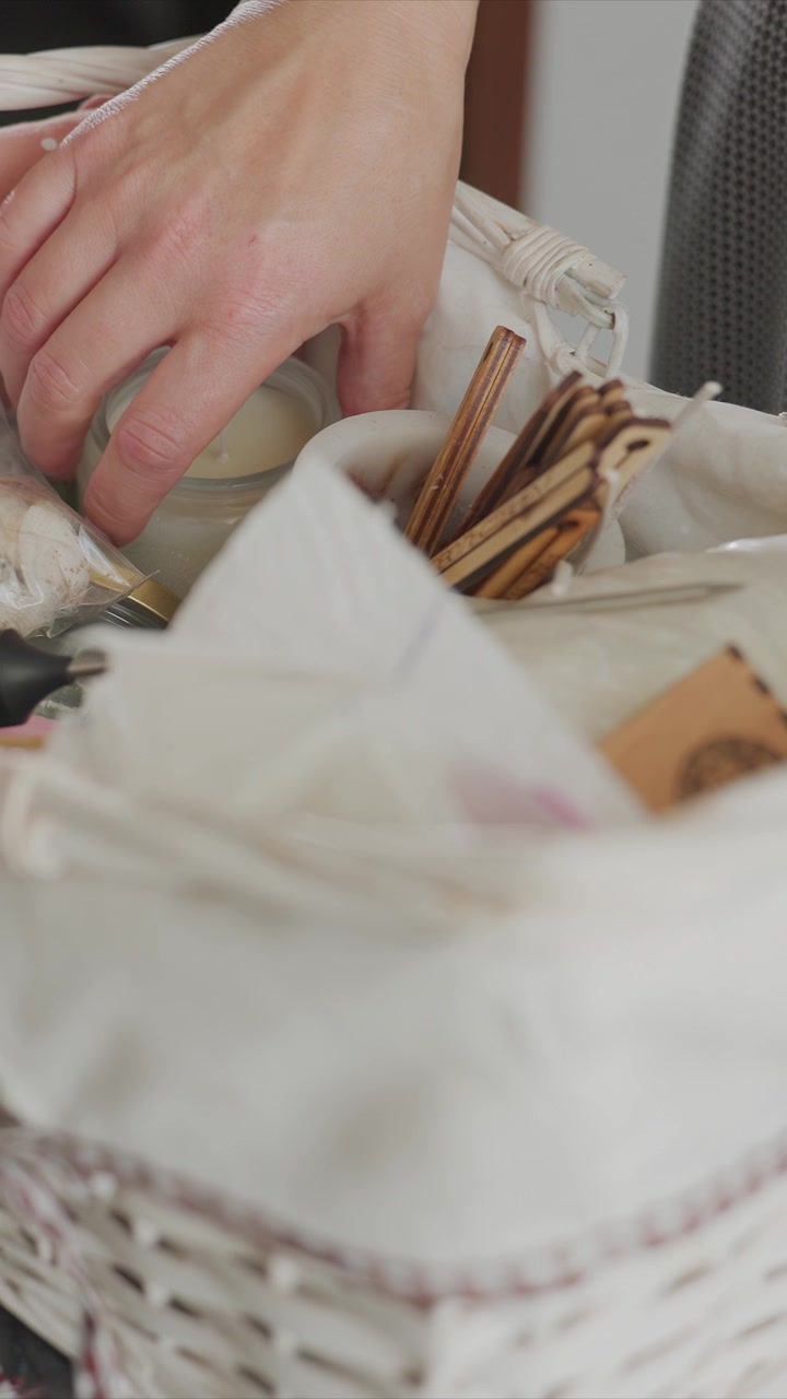 Close up of white woven basket filled with various crafting materials including wooden sticks paper towels and small objects. hand occasionally interacts with items inside basket. scene