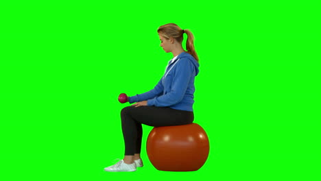 side view of fit woman with dumbbell sitting on exercise ball