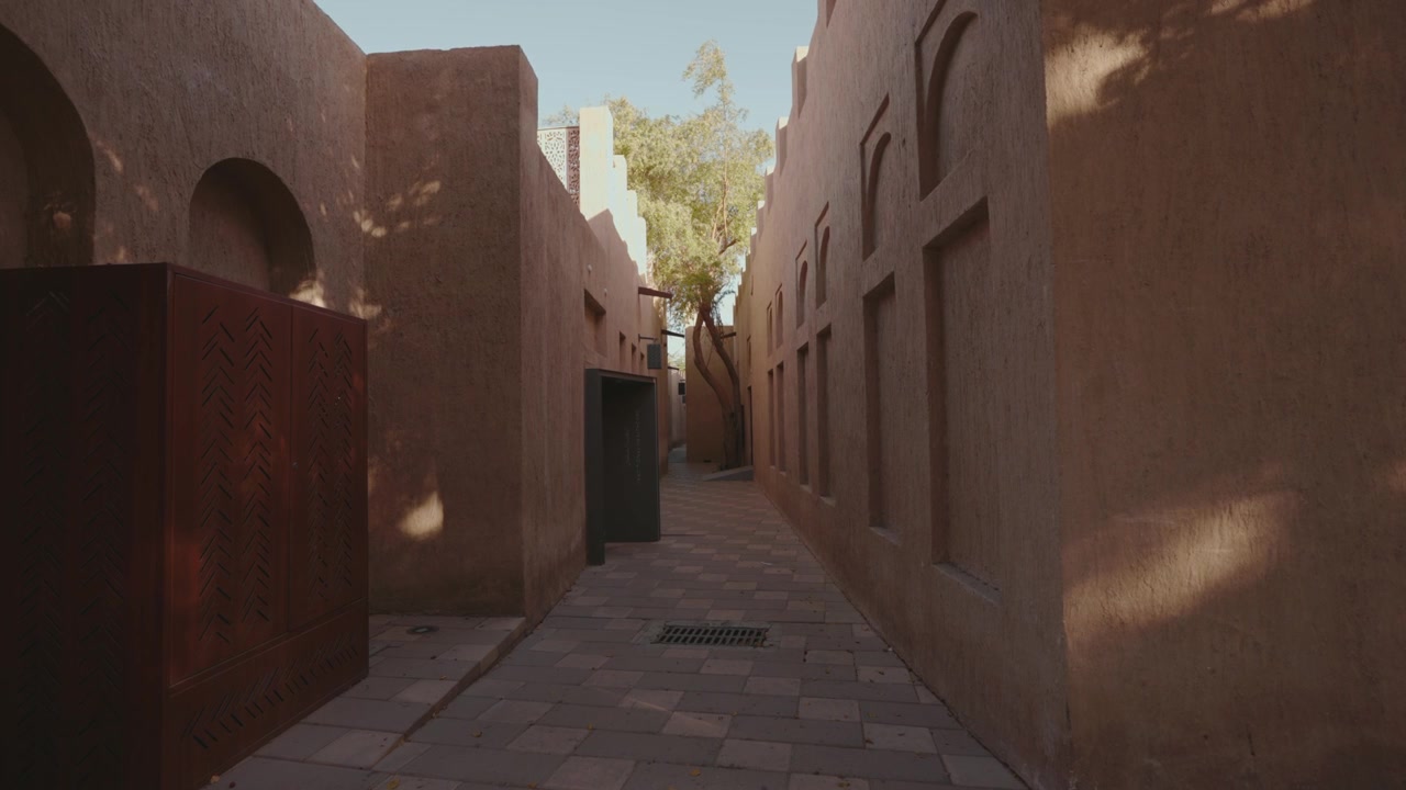 Inquadratura statica di uno stretto vicolo pedonale fiancheggiato da tradizionali muri di terra e portali ad arco in stile architettonico mediorientale. 4K DCI 25fps.