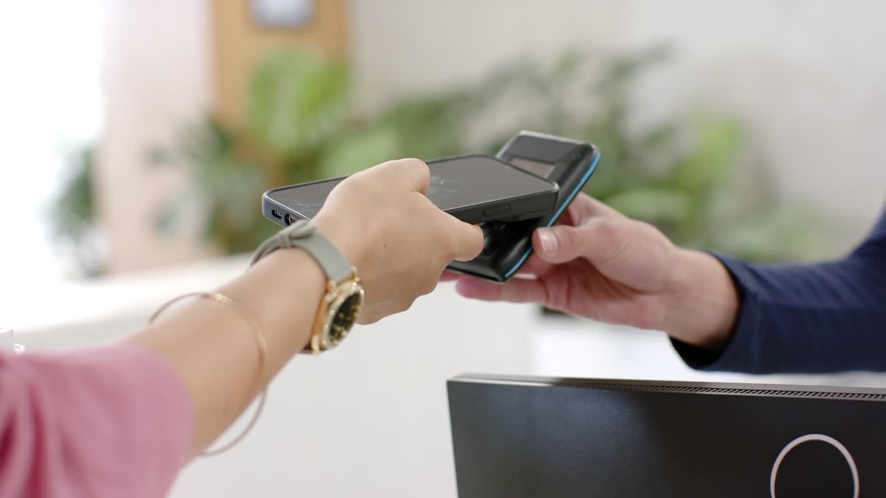 Cliente acercando un smartphone a un lector de tarjetas, personal alineando el terminal y completando el pago en el mostrador