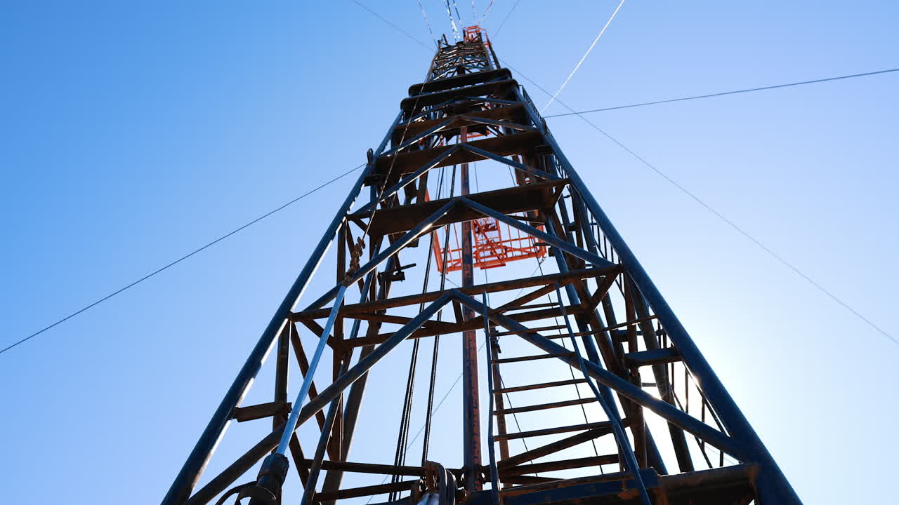 Sun rays pass through the metal tower poles. Low angle view at the derrick for oil production.