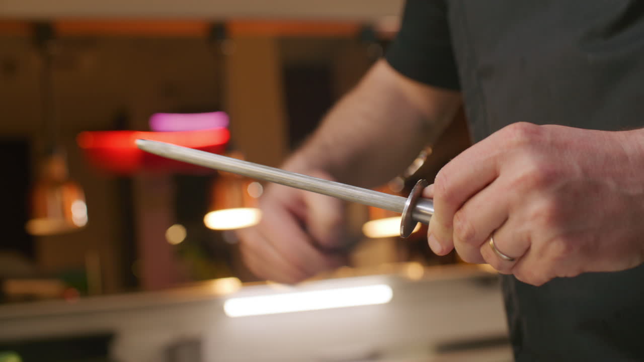 Close Up of Chef Sharpening Knife with Honing Steel in Kitchen