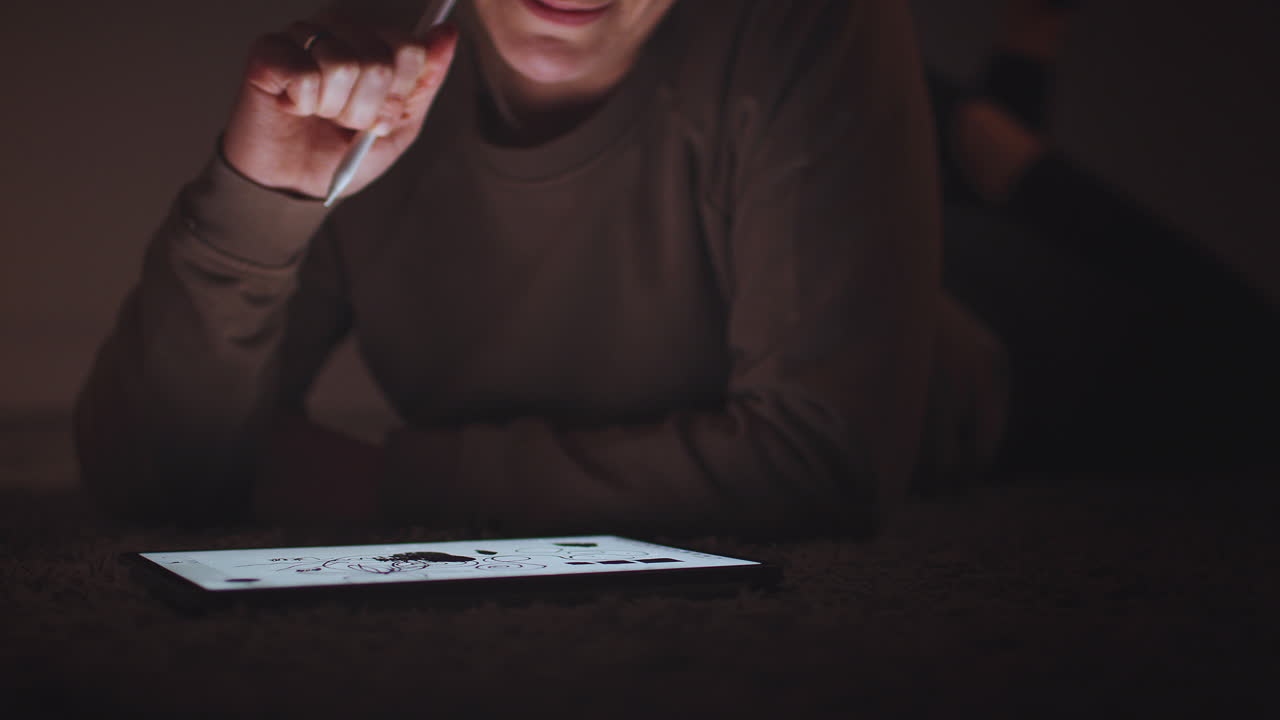 mujer dibujando en una tableta digital usando un bolígrafo por la noche