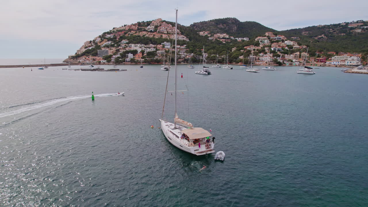 Wide aerial circling a sailboat in the famous Port d'Andratx harbor on the island of Mallorca, Spain, a popular Mediterranean vacation destination for sailing, fishing and dining