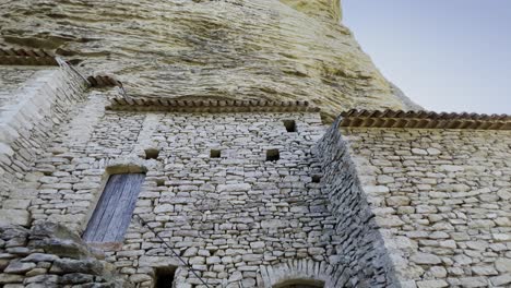 Antigua-Casa-De-Piedra-Hecha-De-Piedras-En-Bruto-Sobre-Una-Roca-Alta-Al-Sol-Con-Viejas-Ventanas-De-Madera,-Abandonada-En-Francia