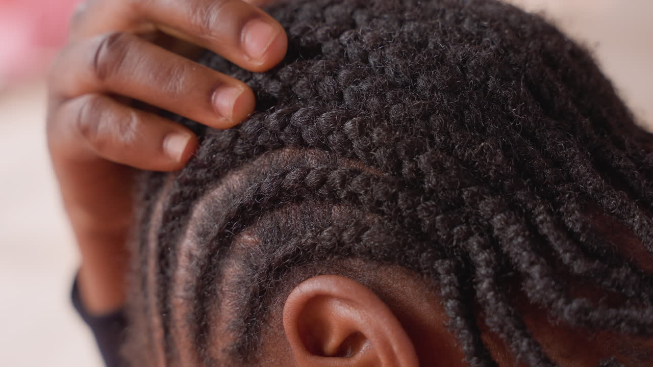 Gros plan d'une jeune fille noire touchant ses tresses collées, rituel de toilettage, doigts doux ajustant les tresses et les rangées tressées, accent sur le cuir chevelu texturé et la coiffure protectrice, moment intime de soin capillaire à la maison pour la beauté