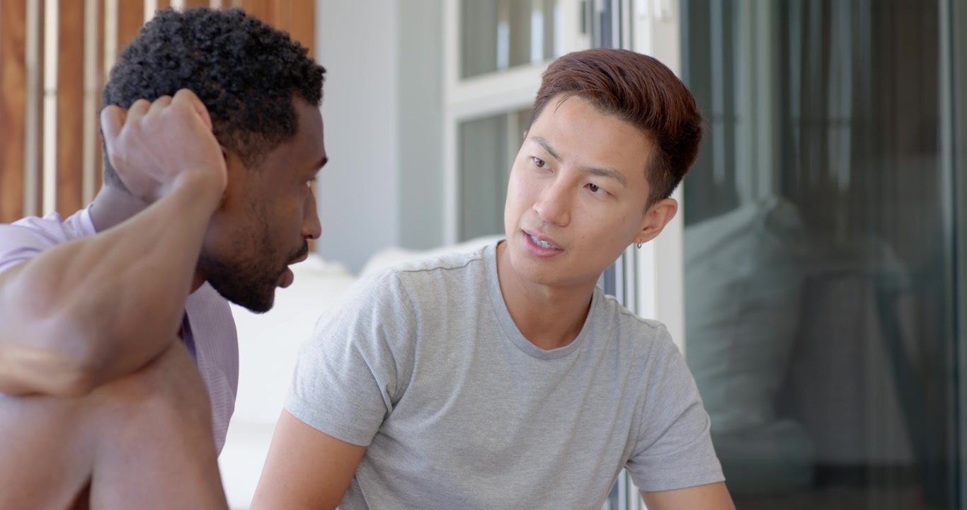 パティオに座っている多様な男性たち。アジア人男性はスマートフォンを持ち、左側の男性が話すのを聞いている。