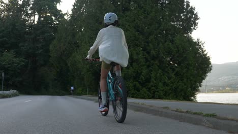 Following-A-Woman-Biking-In-The-Road-Along-The-Burrard-Inlet-In-Vancouver,-Canada