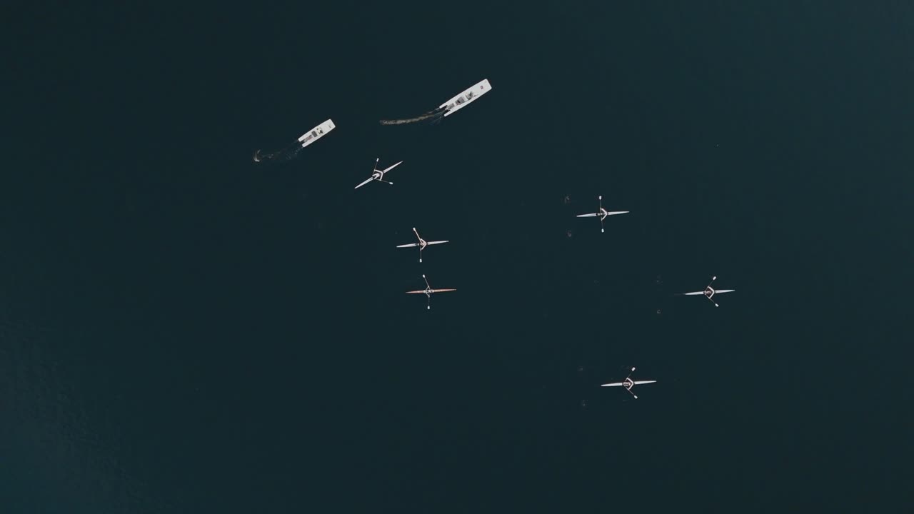 tiro de seguimiento de ojo de pájaro de remeros entrenando en un lago con entrenadores instruyendo desde lanzamientos