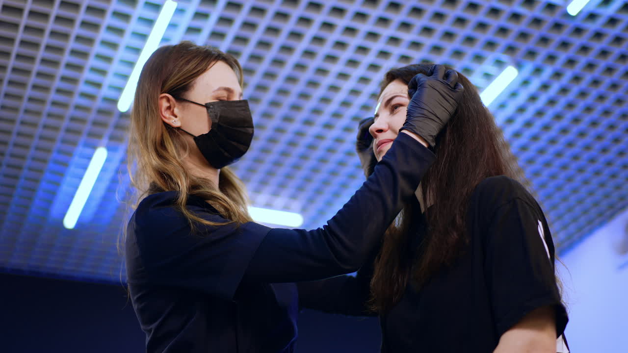 Positive women in a beauty salon. Beautician prepares the client for permanent eyebrow make up. Low angle view.