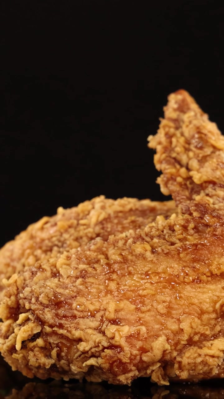 Golden, crispy fried chicken wings rotate smoothly on a glossy black surface under studio lighting, highlighting texture and detail with a dramatic, appetizing mood