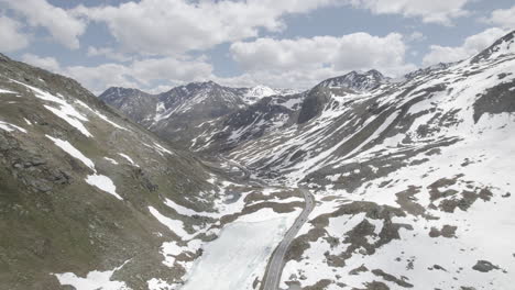 Drone-shot-flying-over-a-single-road-in-between-snow-mountains-at-the-Fluela-Pass-in-Switzerland-on-a-cloudy-and-cold-day-with-clear-sight-LOG