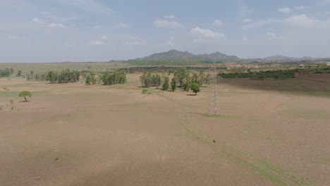 Aerial---Forward-drone-flyby-power-line-towards-hilly-outcrop-on-cloudy-day