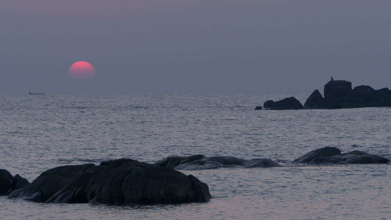 일몰, 카나코나, 고아, 인도에서 암석에서 낚시하는 실루엣 보트와 어린 아이