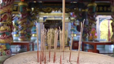 close-up group of joss sticks in a big pot, with blurred background of a chinese temple or shrine