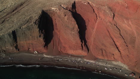 aerial view of red beach, santorini island, greece, people on sandy coast under steep cliffs