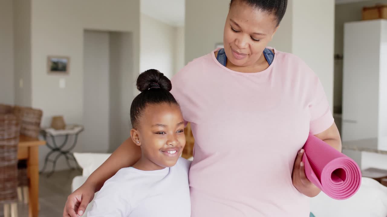 Happy unaltered african american mother and daughter holding yoga mats and smiling, slow motion