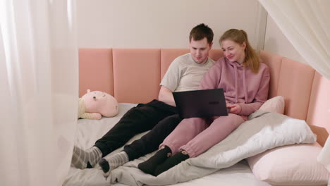 couple relaxing on bed, watching laptop