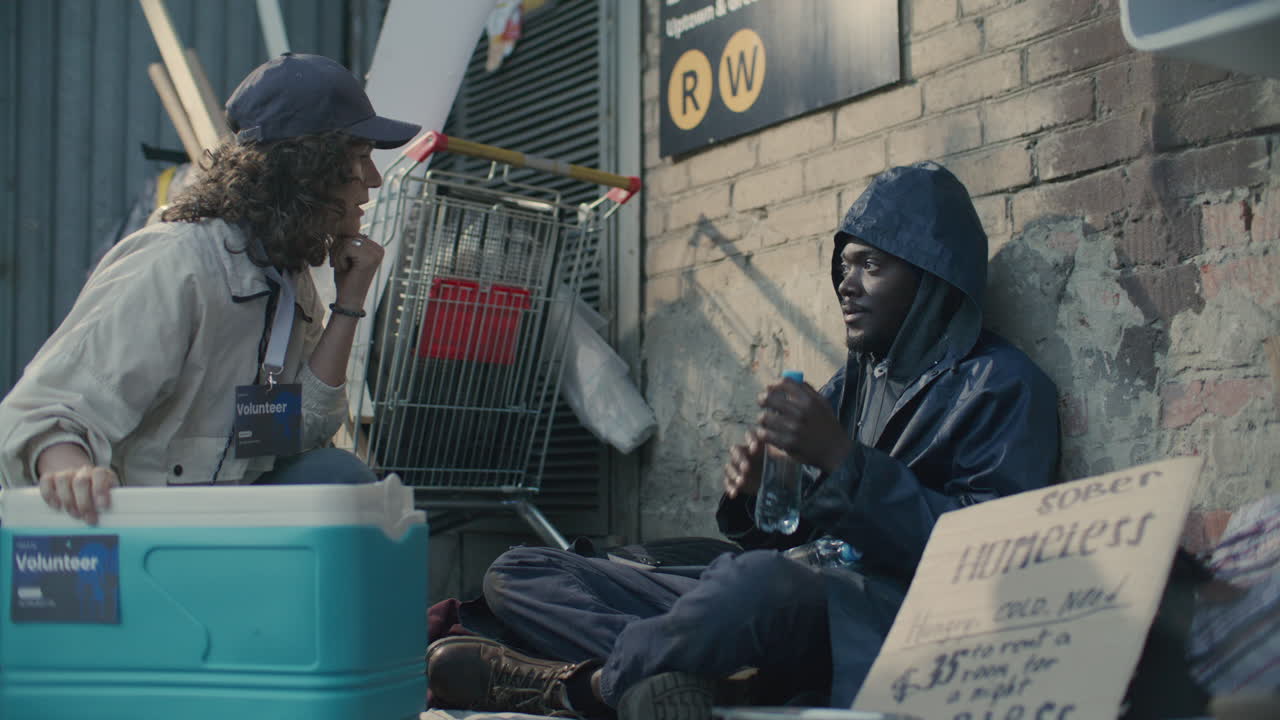 Volunteer Giving Water Bottles and Talking to Homeless Man on Street
