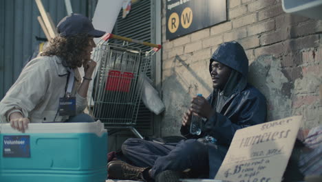 volunteer giving water bottles and talking to homeless man on street