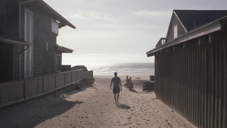 static shot of boy walking towards beach on a path between two houses at cannon beach, oregon