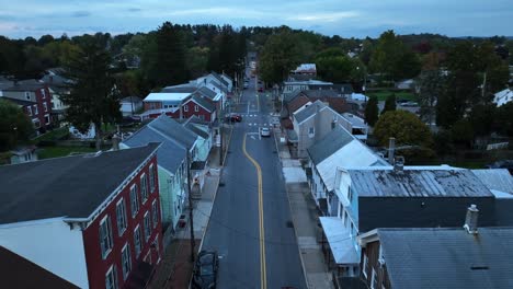 twilight over a quiet, small-town street lined with traditional houses and cars