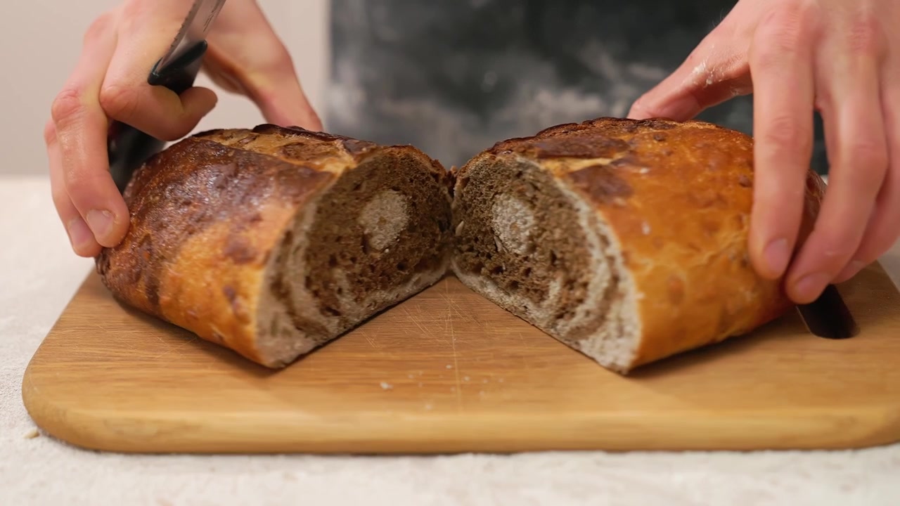 Persona che affetta una pagnotta di pane marmorizzato appena sfornata.