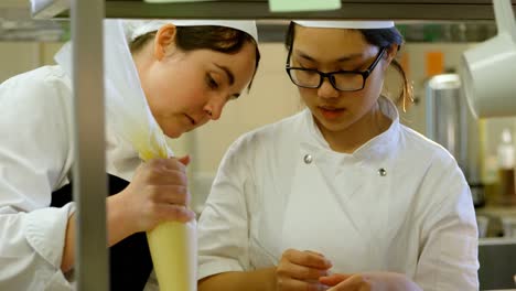 female chef icing muffins with pastry bag in kitchen 4k