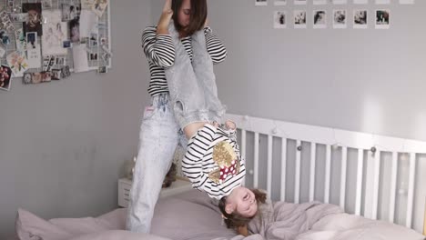 Brown-haired-mother-and-daughter-having-fun-in-bed-and-turning-her-upside-down-and-swinging.-Slow-motion