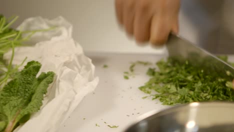 Close-up-of-hands-finely-chopping-fresh-herbs-on-a-kitchen-counter,-with-camera-panning-to-follow-the-action