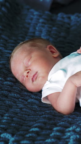beautiful newborn caucasian baby in white bodysuit. tiny child sleeping on the blue blanket. close up. vertical video