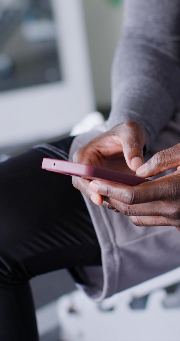 Vertical video: Man wearing grey top holding pink-cased smartphone, tapping and swiping near window
