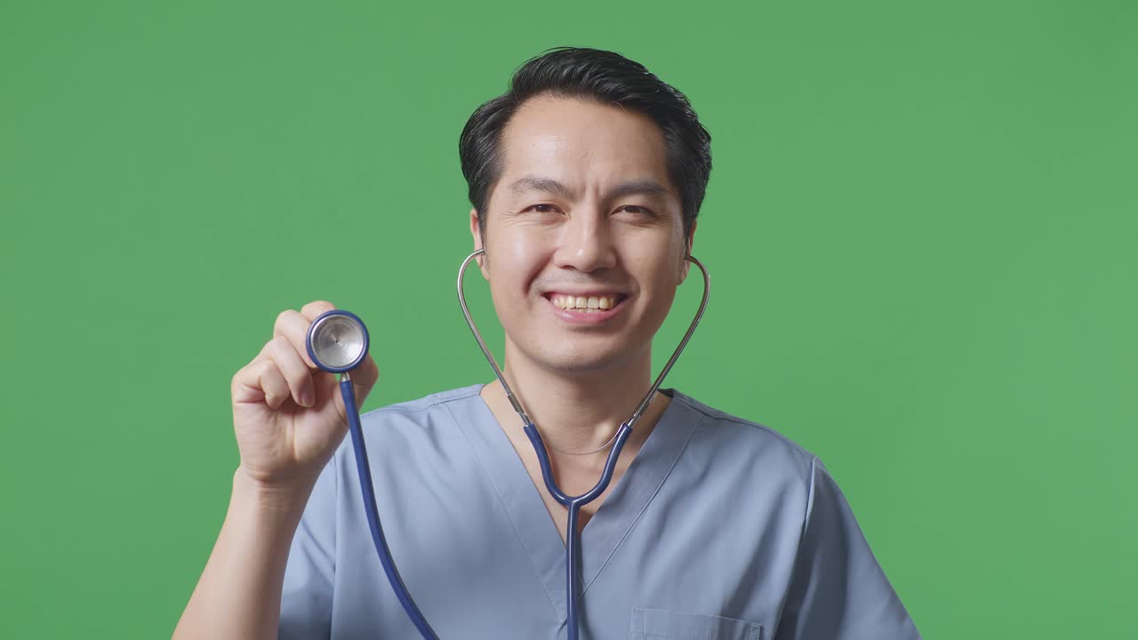 아시아 남성 의사가 미소 짓고 스테토스코프를 사용하면서 병원에서 녹색 화면 배경에 서 있습니다.