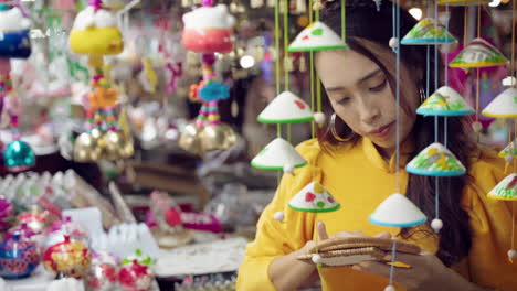 Mujer-Joven-En-Amarillo-Ao-Dai-Admirando-Artesanías-En-El-Mercado-De-Hoi-An,-Colores-Vibrantes,-Primer-Plano