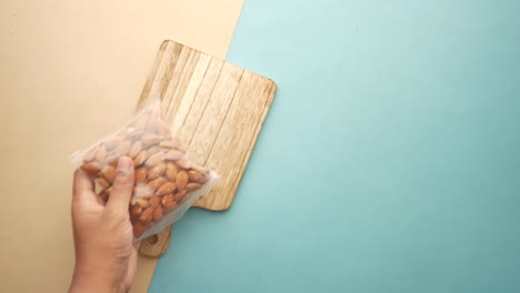 hand holding a bag of almonds on a wooden cutting board.