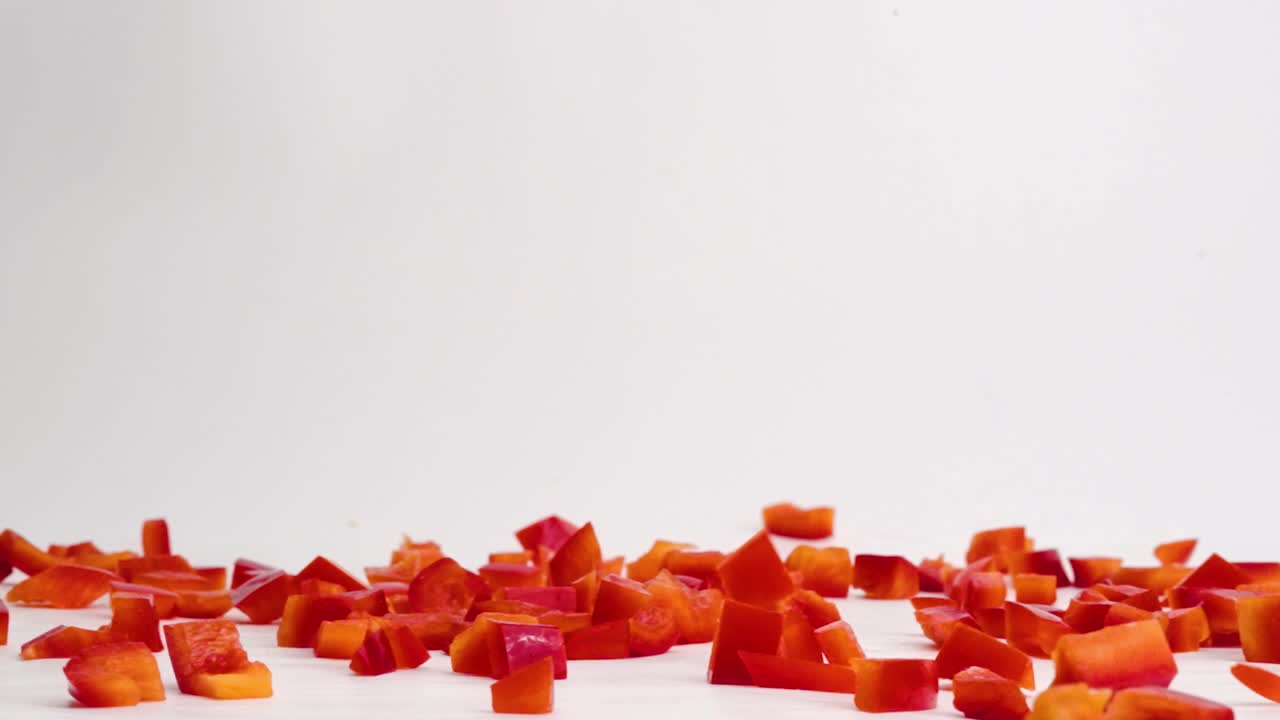 Cubetti di peperone rosso brillante che cadono e rimbalzano su un tavolo bianco, ammucchiandosi al rallentatore