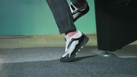 close-up shot of male leg wearing stylish white and black sneakers with grey plaid trousers. foot slightly lifted off grey carpeted floor, creating a dynamic fashion statement with modern