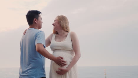 Happy-Young-Couple-By-The-Sea---Caucasian-Pregnant-Woman-And-Her-Asian-Husband