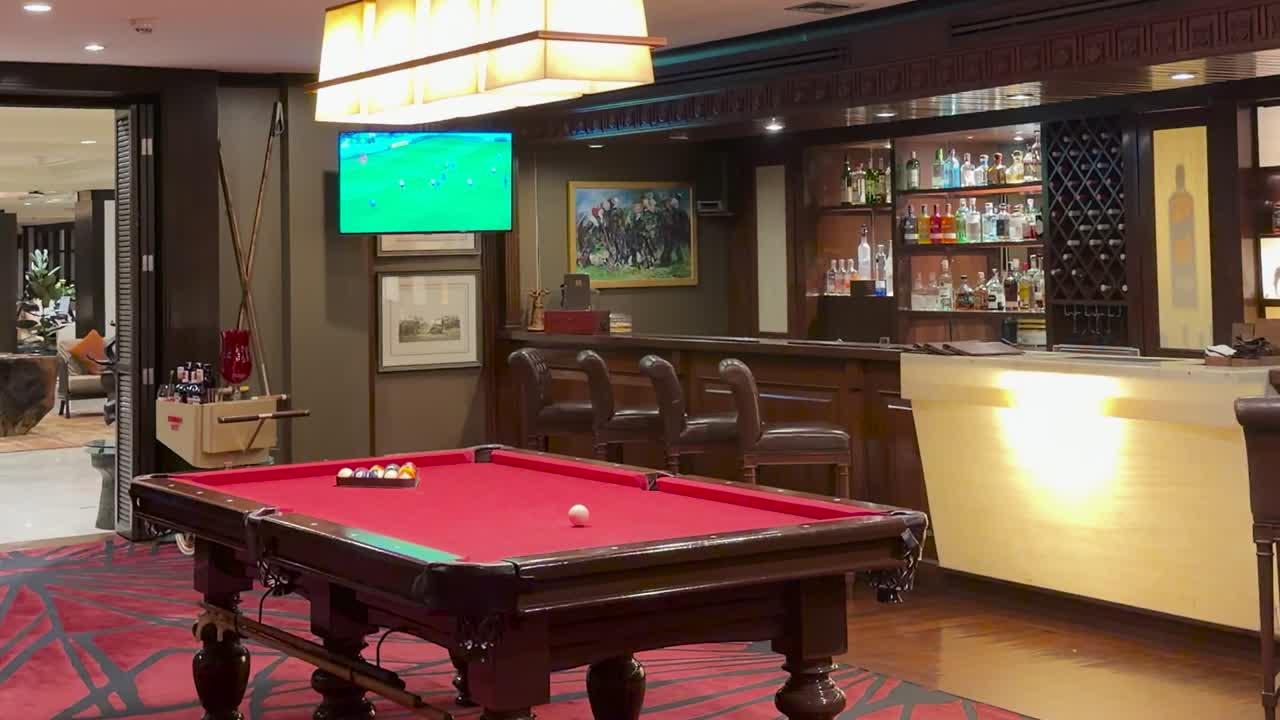 Elegant lounge featuring a red pool table, illuminated bar counter, and warm evening lighting