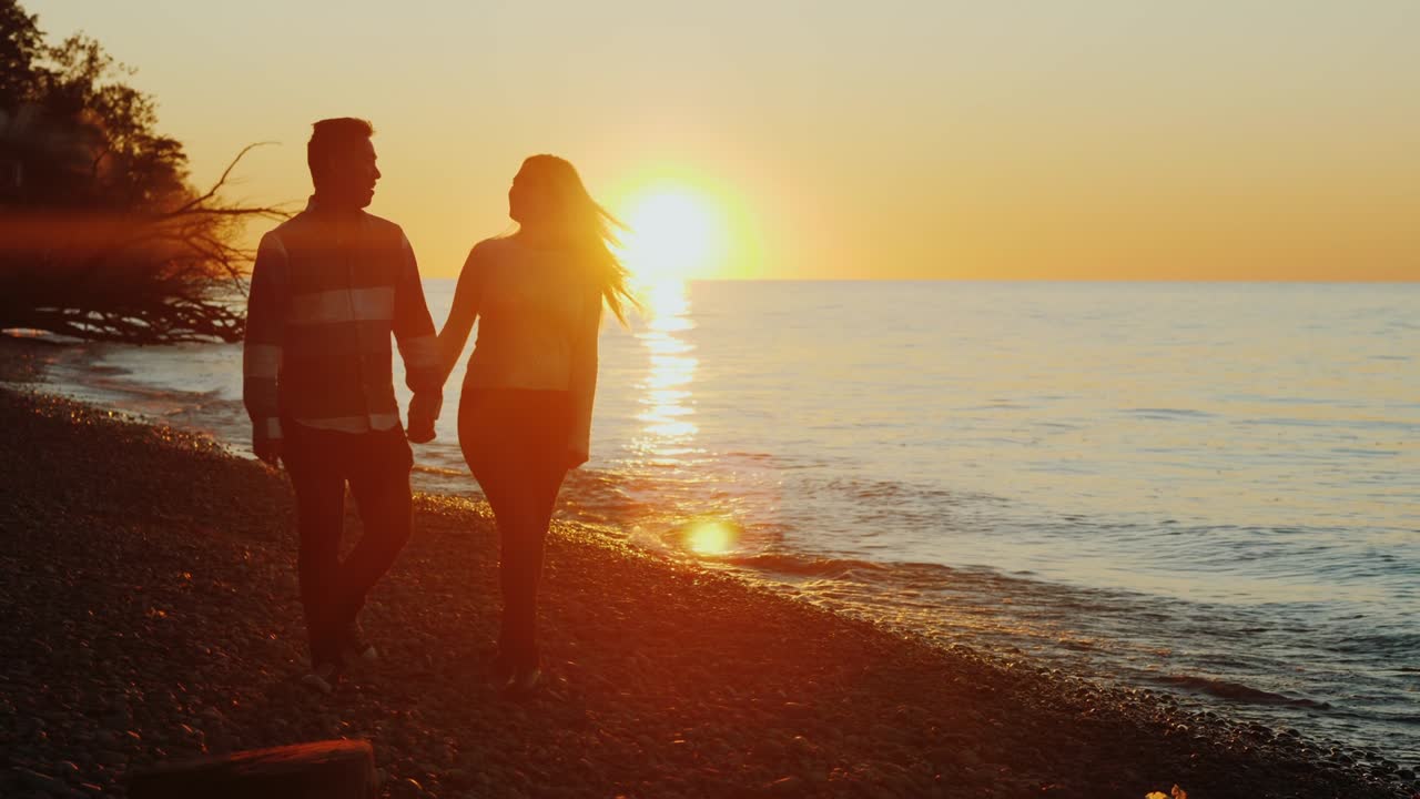 스테디캠 : 손을 잡고 해가 지는 해변을 따라 는 젊은 다민족 부부.