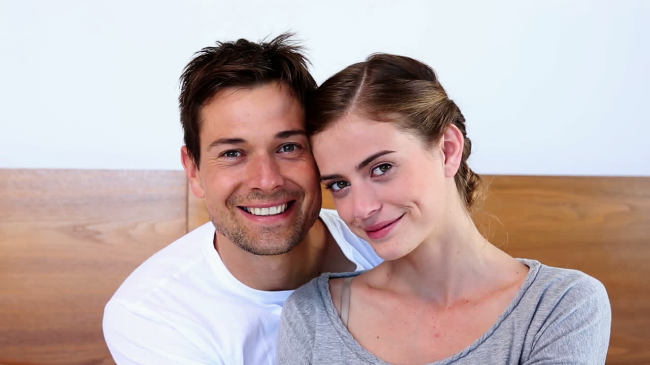 Casal feliz sentado na cama, sorrindo para a câmera