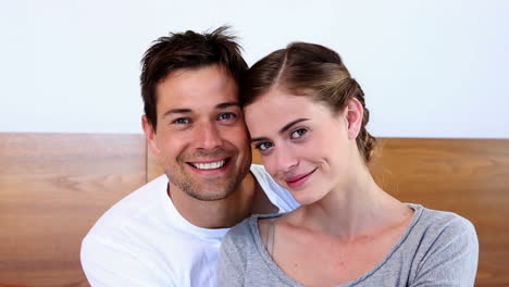 Happy-couple-sitting-on-bed-smiling-at-camera