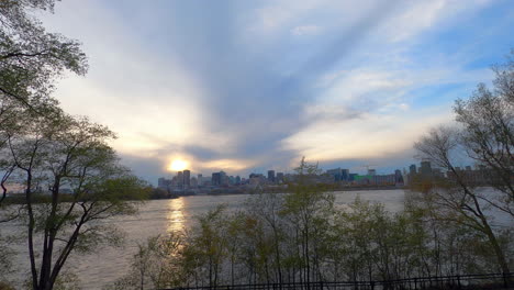 timelapse montreal at beautiful golden sunset, waterfront sightseeing view of st-lawrence river, water flow, trees, cloudy sky and downtown buildings in background