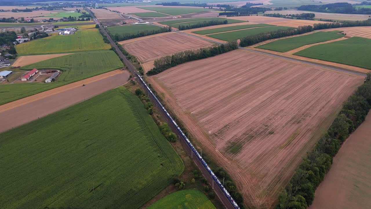 Train carrying luxury new cars for sale. Transportation of heavy cargo from aerial view. Long wagons on tracks in rural environment