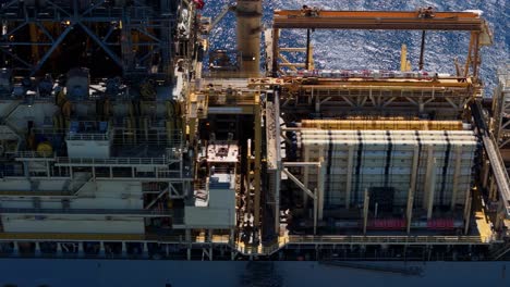 aerial top-down pan across the bustling cargo ship by oil rig platform with industrial machinery and equipment across deck